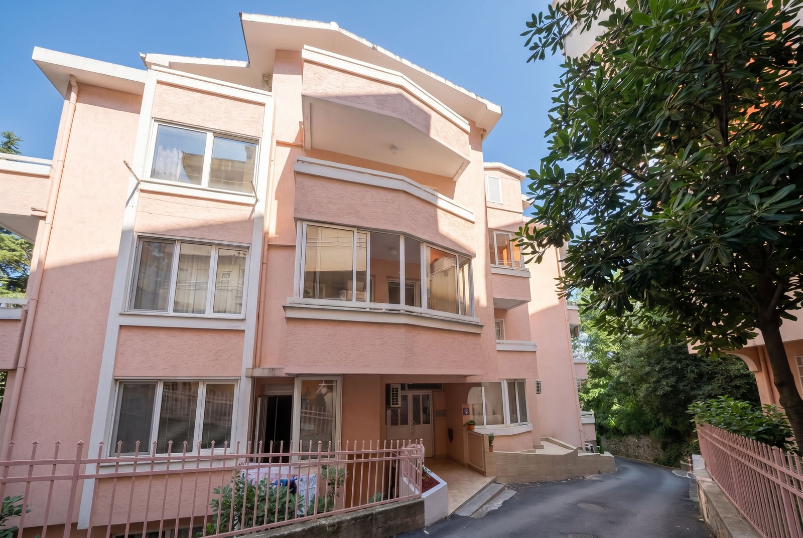 Facade of a three-story peach-colored residential building in Budva, Montenegro, with panoramic windows and a metal fence.