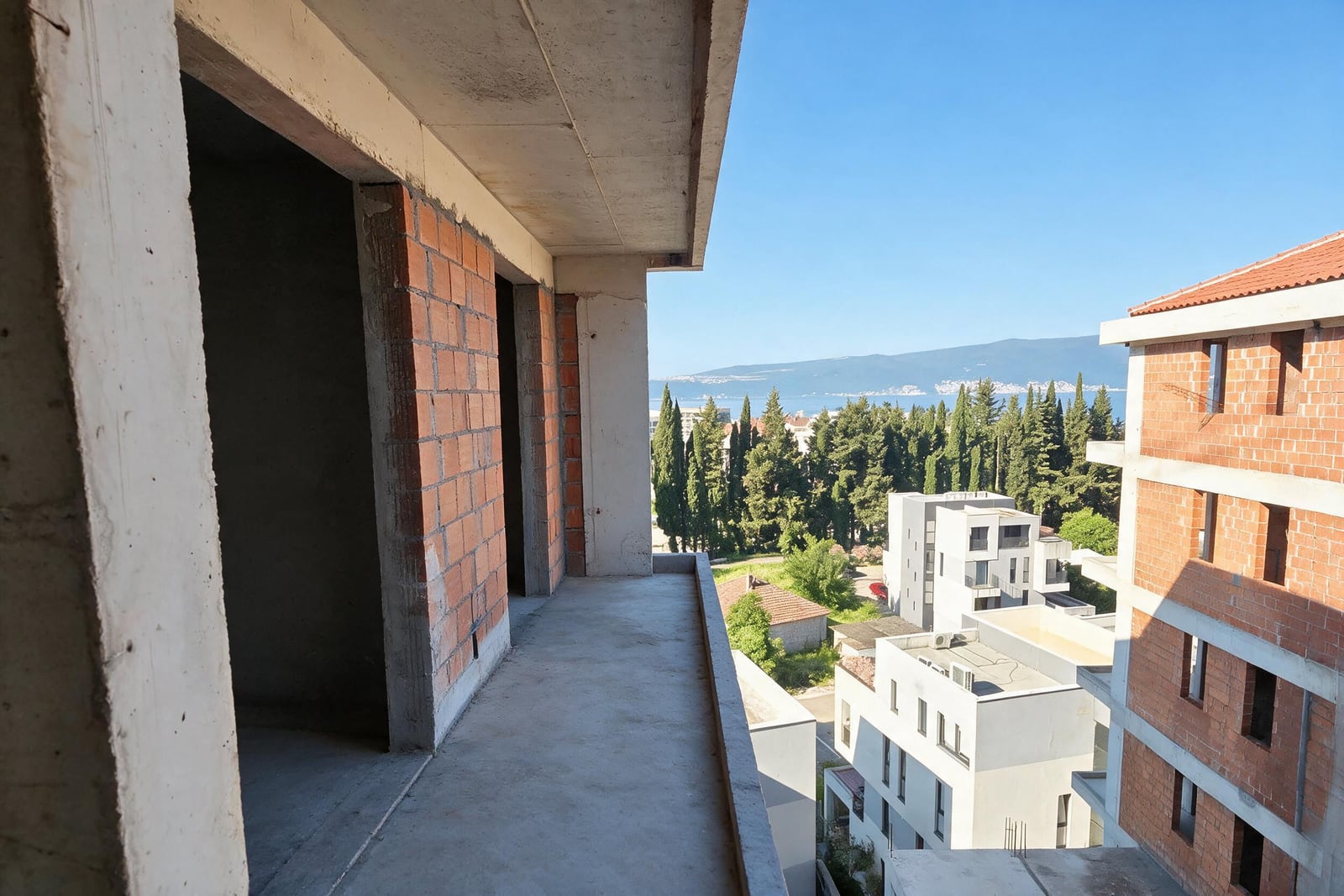 View from the open balcony of a building under construction overlooking the sea and mountains in Tivat, Montenegro.