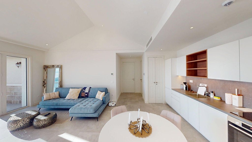 Modernes Wohnzimmer mit Küche in der Wohnung Lustica Bay, Montenegro: blaues Sofa, weiße Möbel und Zugang zur Terrasse.