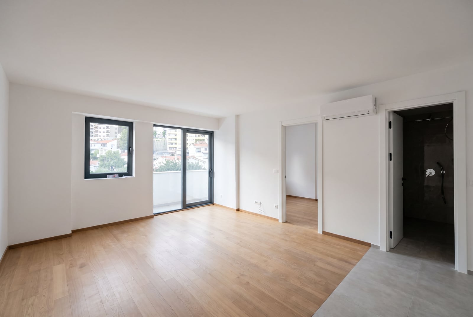 Bright empty living room with parquet flooring, panoramic window, and air conditioning in a new apartment in Budva, Montenegro.