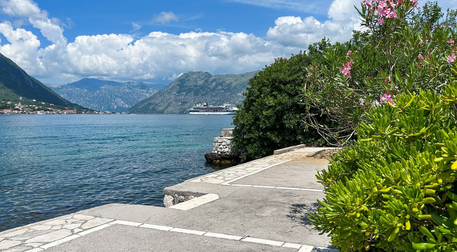 Blick auf die Bucht von Kotor von der Terrasse der Villa in Dobrota, Montenegro: Steinpromenade, Berge und ein Kreuzfahrtschiff.