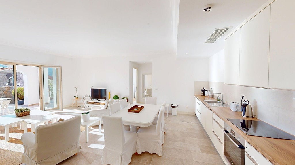 Helles Wohnzimmer mit Küche im modernen Stil in der Apartmentsiedlung Luštica, Montenegro: weiße Möbel und Zugang zur Terrasse.