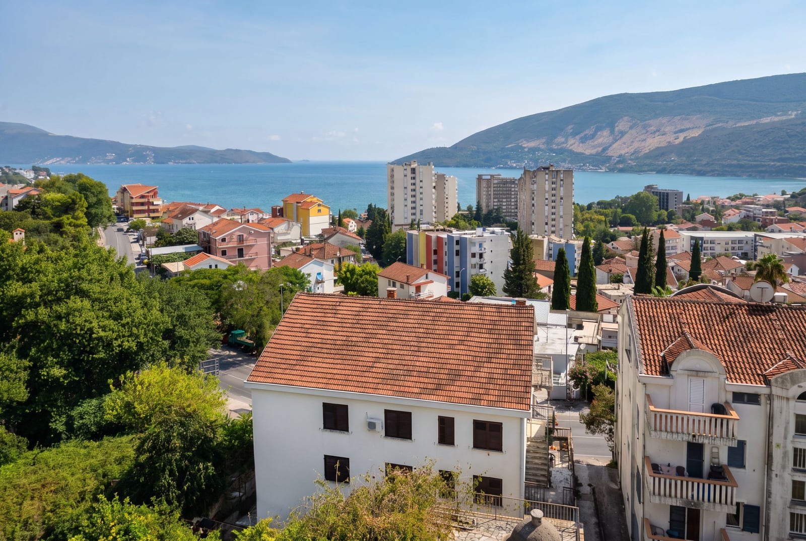 Panoramic view of the sea, tiled roofs, and mountains from an apartment in Igalo, Montenegro.