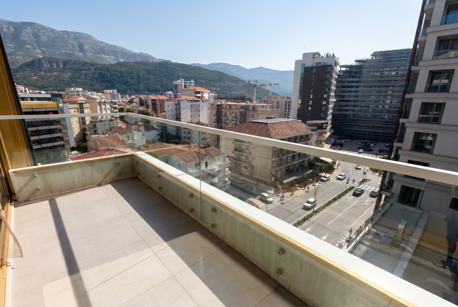 View from the balcony of a modern apartment in Budva, Montenegro: city panorama, mountain landscape, and glass railing.