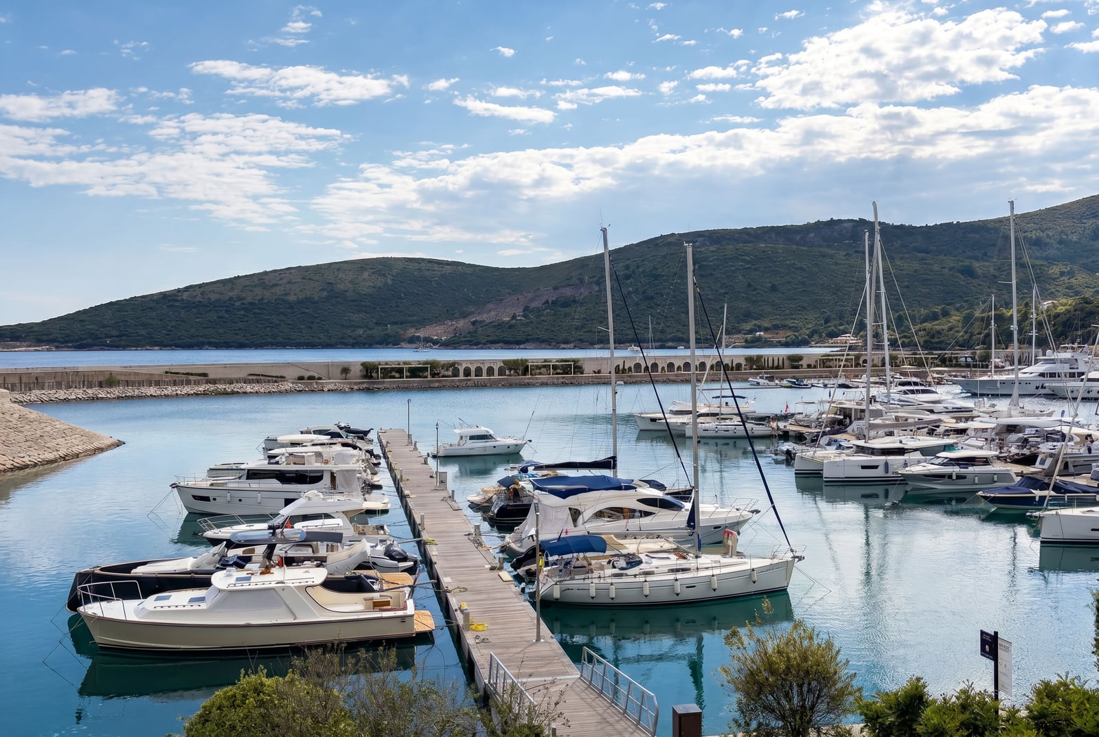 Blick auf den Yachthafen in Luštica Bay, Montenegro: Anlegestelle mit schneeweißen Yachten vor der Kulisse der Berge und der Adria.