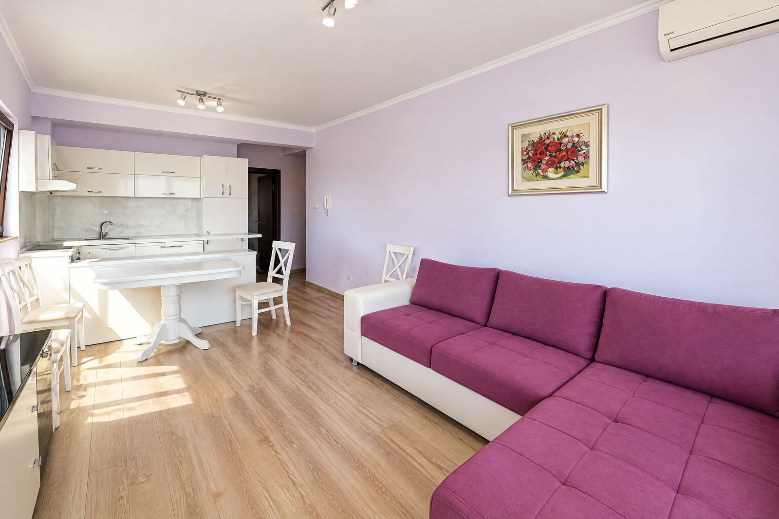 Spacious living room with kitchen in an apartment in Budva, Montenegro: pink corner sofa, white furniture, and laminate flooring