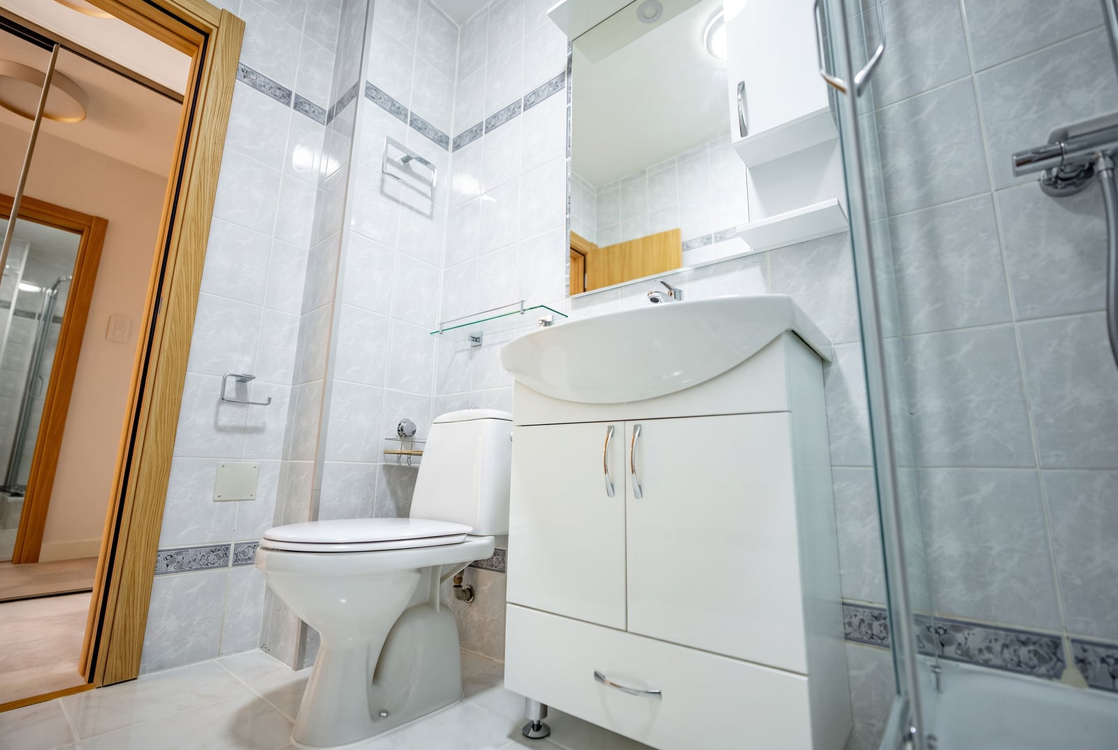 Bright bathroom with a shower cabin in an apartment, Sveti Stefan, Montenegro: white tiles, vanity unit with sink and mirror.