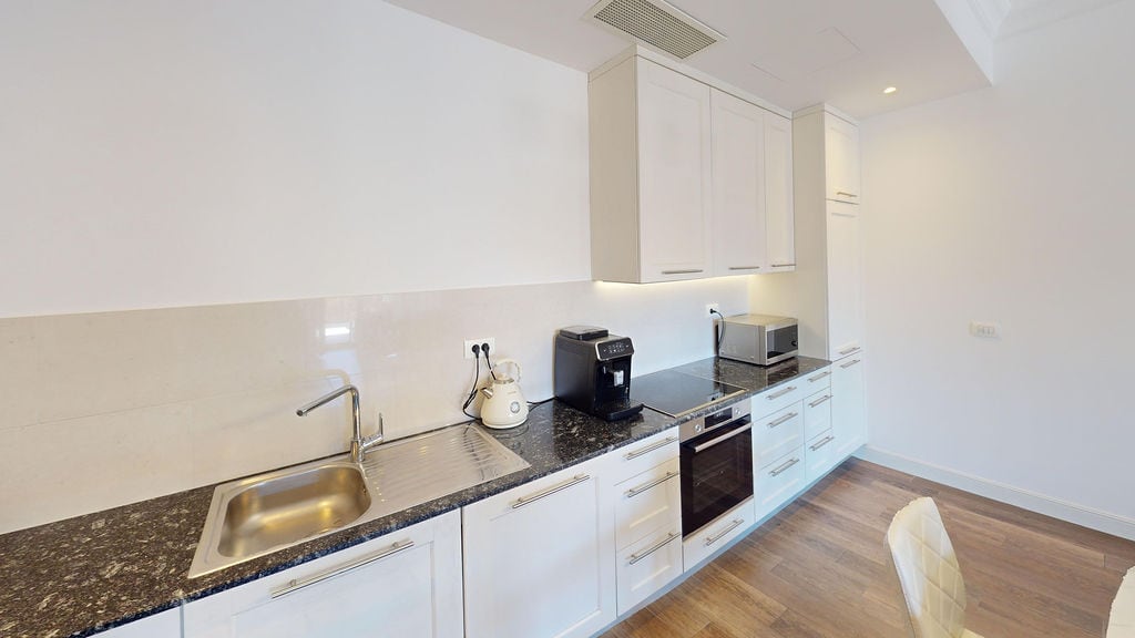 Moderne weiße Küche mit dunkler Arbeitsplatte in einer Wohnung der Wohnanlage Luštica, Montenegro: eingebaute Geräte und helles Interieur.