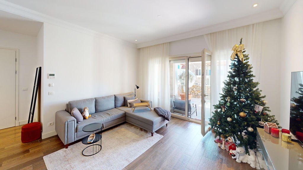 Karadağ, Luštica Konutları'ndaki bir dairede gri kanepe ve Noel ağacı bulunan aydınlık oturma odası. Terasa çıkışlı, modern iç mekan.
