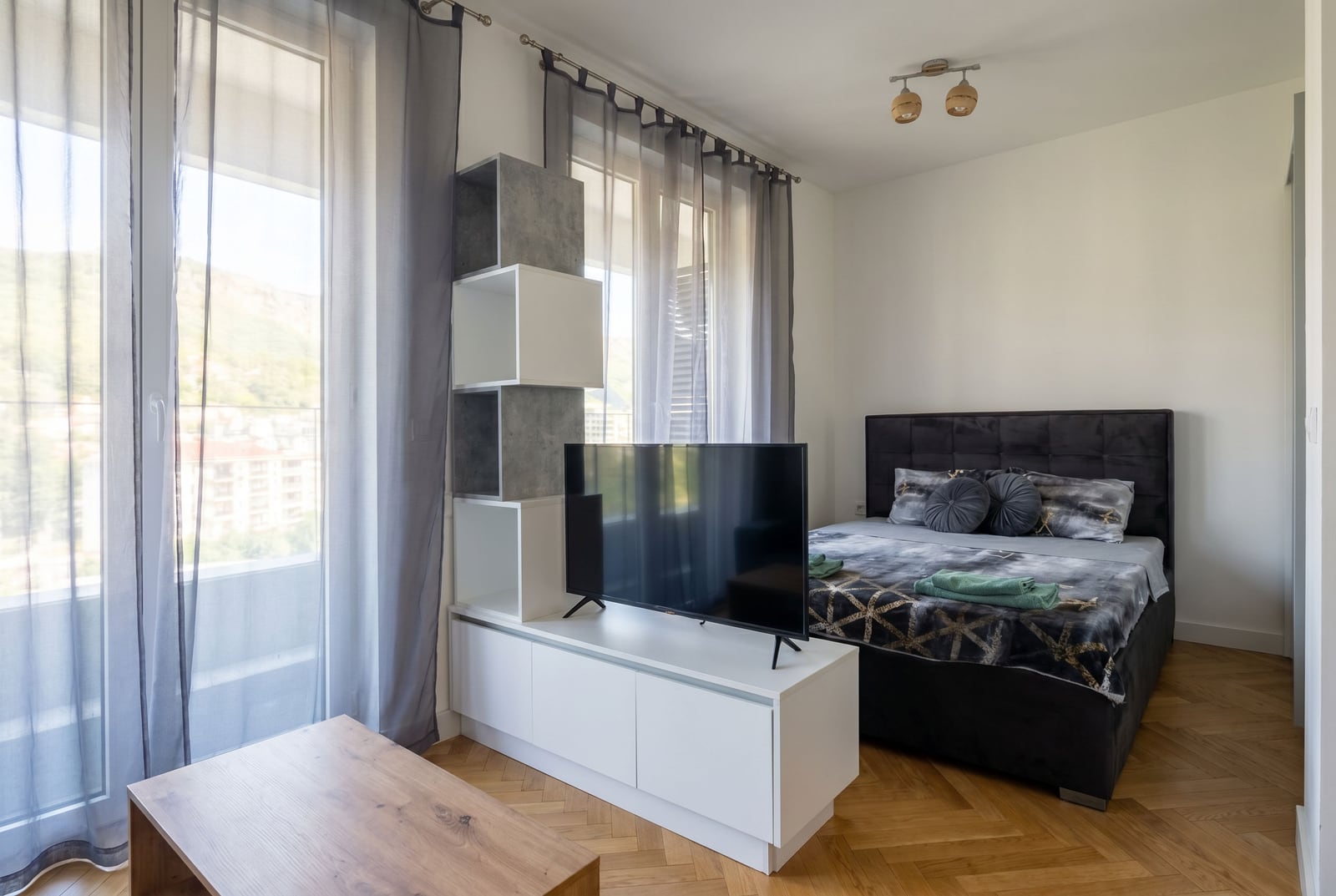 Moderna spavaća soba sa bračnim krevetom i TV zonom u stanu u Bečićima, Crna Gora, sa pogledom na planine.