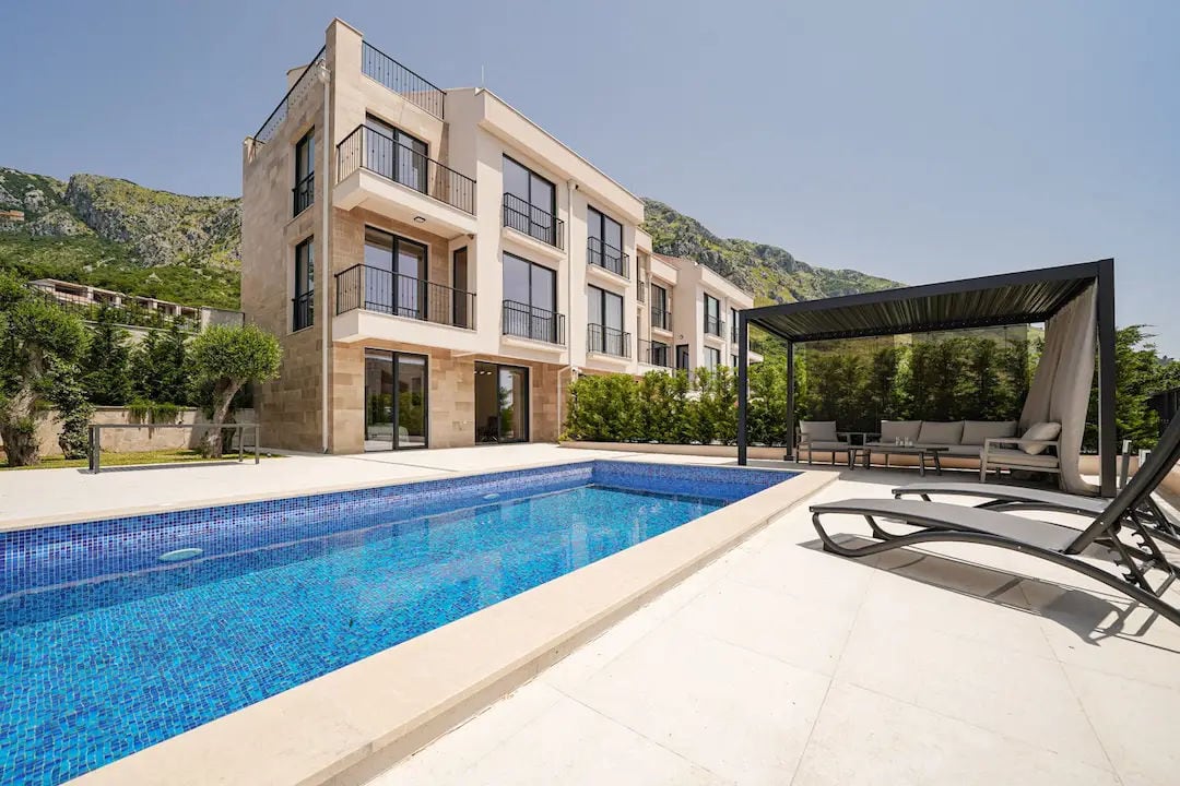 Modern villa in Reževići, Montenegro: outdoor swimming pool, terrace with sun loungers, and a lounge area against a mountain backdrop.