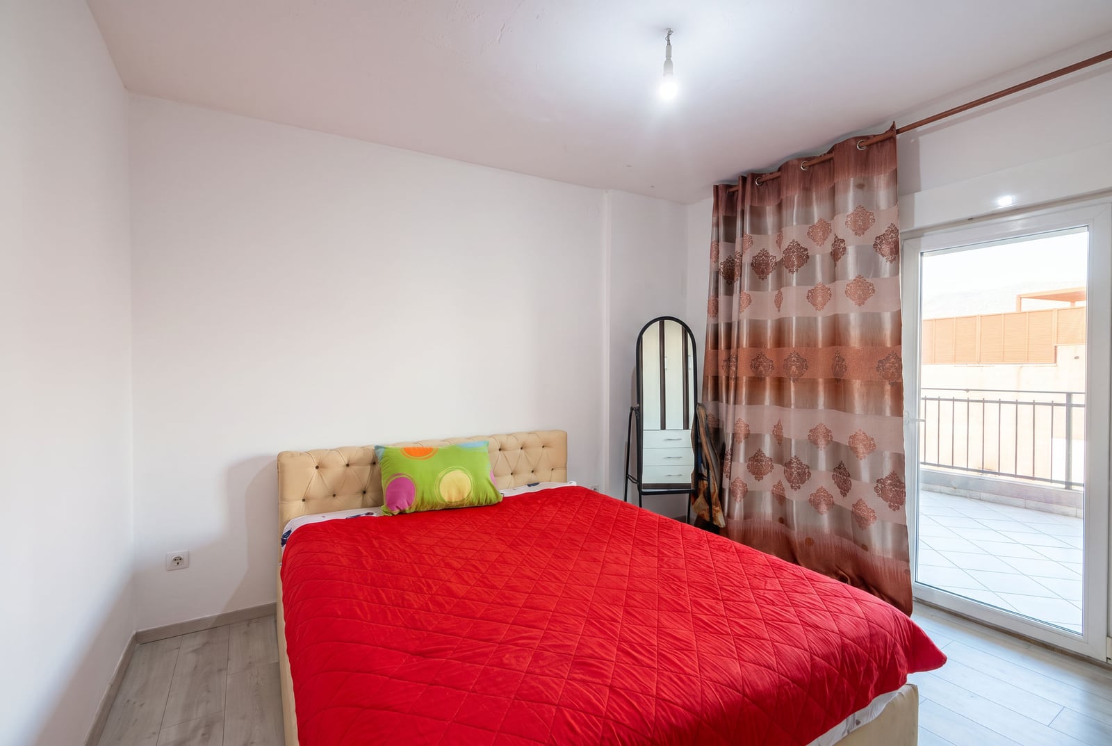 Svetla spavaća soba sa bračnim krevetom, crvenim prekrivačem i izlazom na balkon u stanu u Budvi, Crna Gora