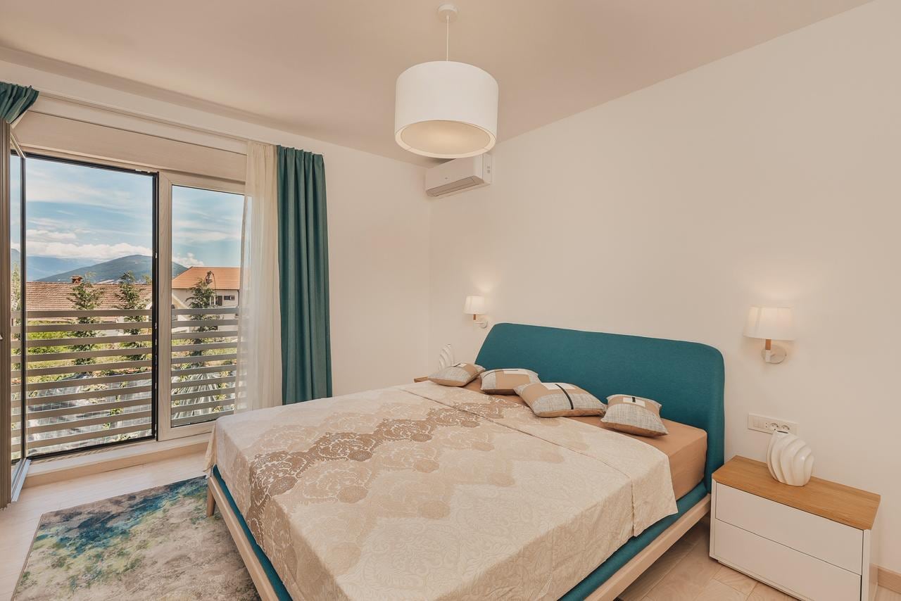 Helles Schlafzimmer mit Doppelbett und Zugang zum Balkon mit Bergblick in einer Wohnung in Igalo, Montenegro.