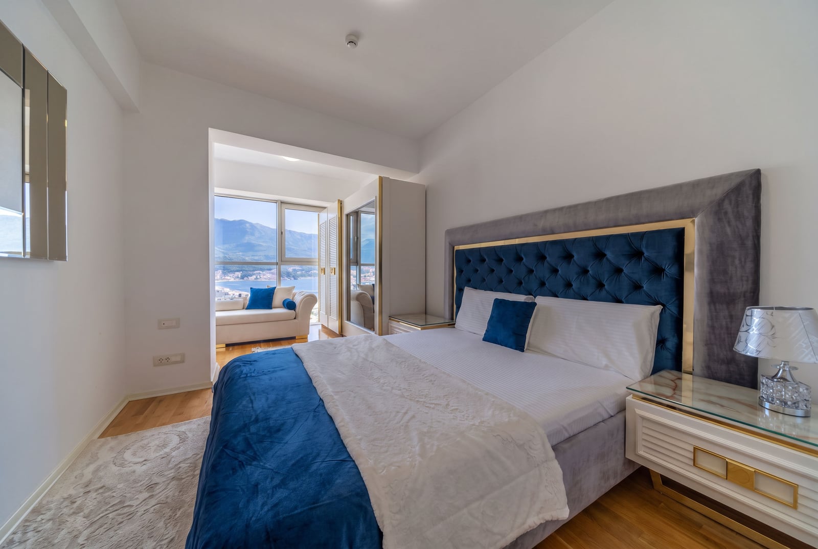 Modern bedroom with a blue bed, panoramic window, and sea view in an apartment in Bečići, Montenegro