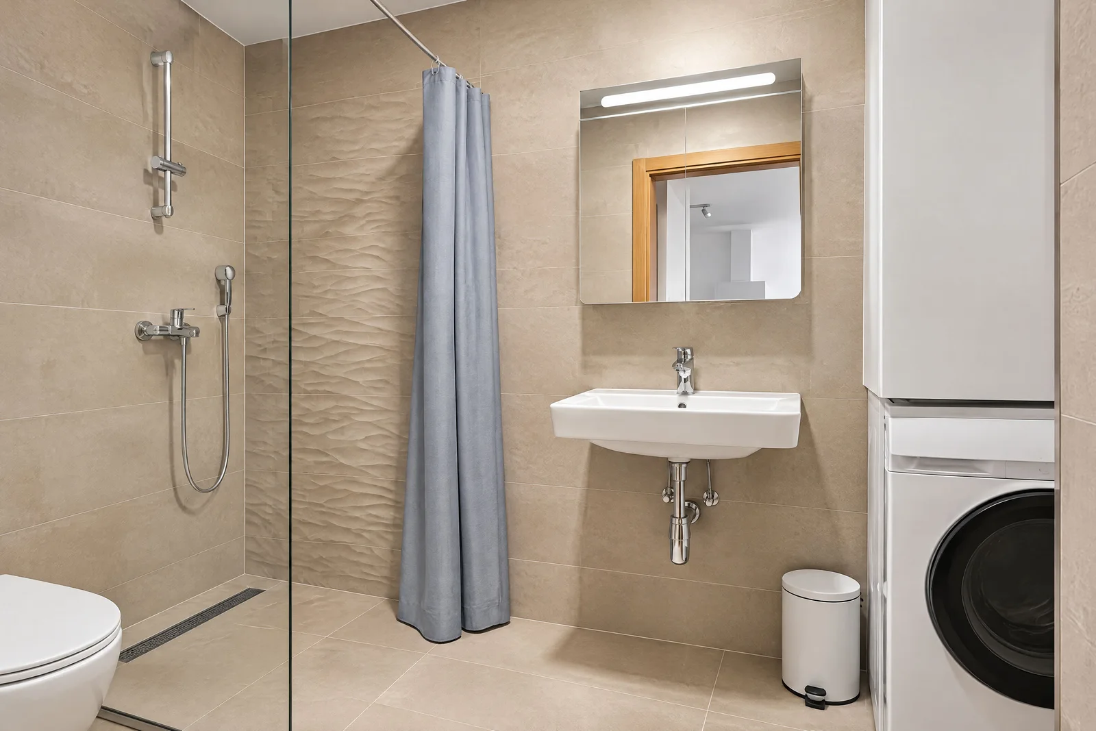 Duş perdesi, duvar monteli lavabolu, aydınlatmalı mirrorlu ve çamaşır makinelı bej banyo.