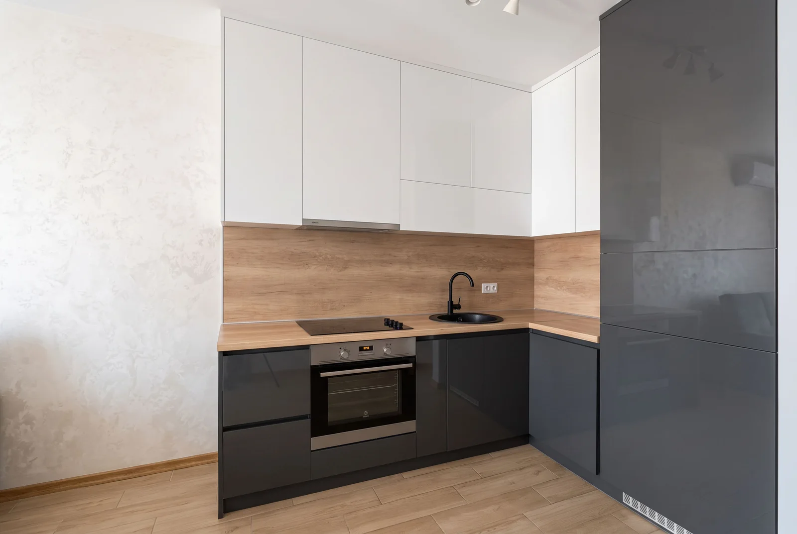 Modern kitchen featuring grey and white cabinets, wood countertops, built-in oven, black sink, and induction cooktop.