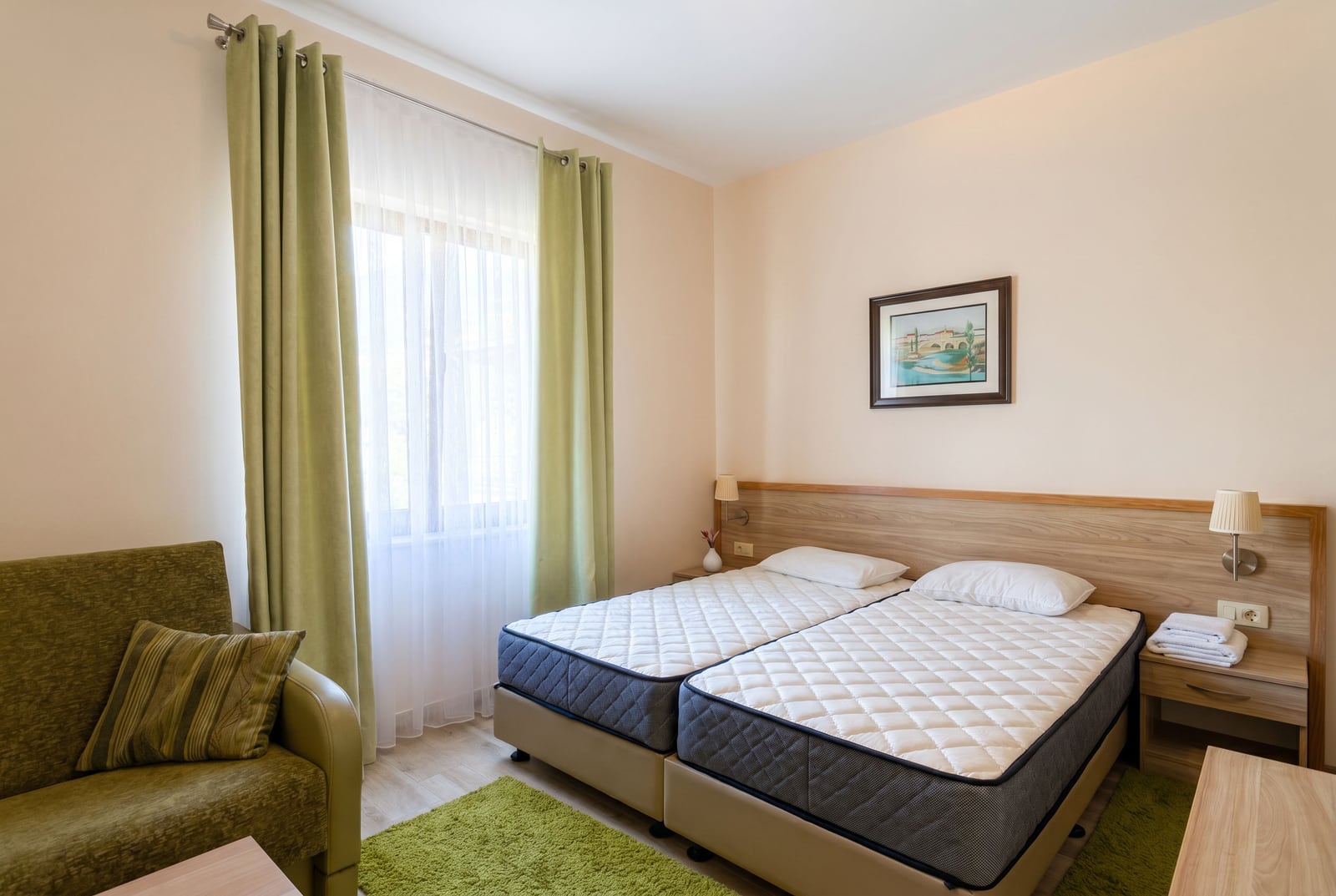 Cozy bedroom with two beds, a green sofa, and light-toned finishes in an apartment in Bečići, Montenegro.