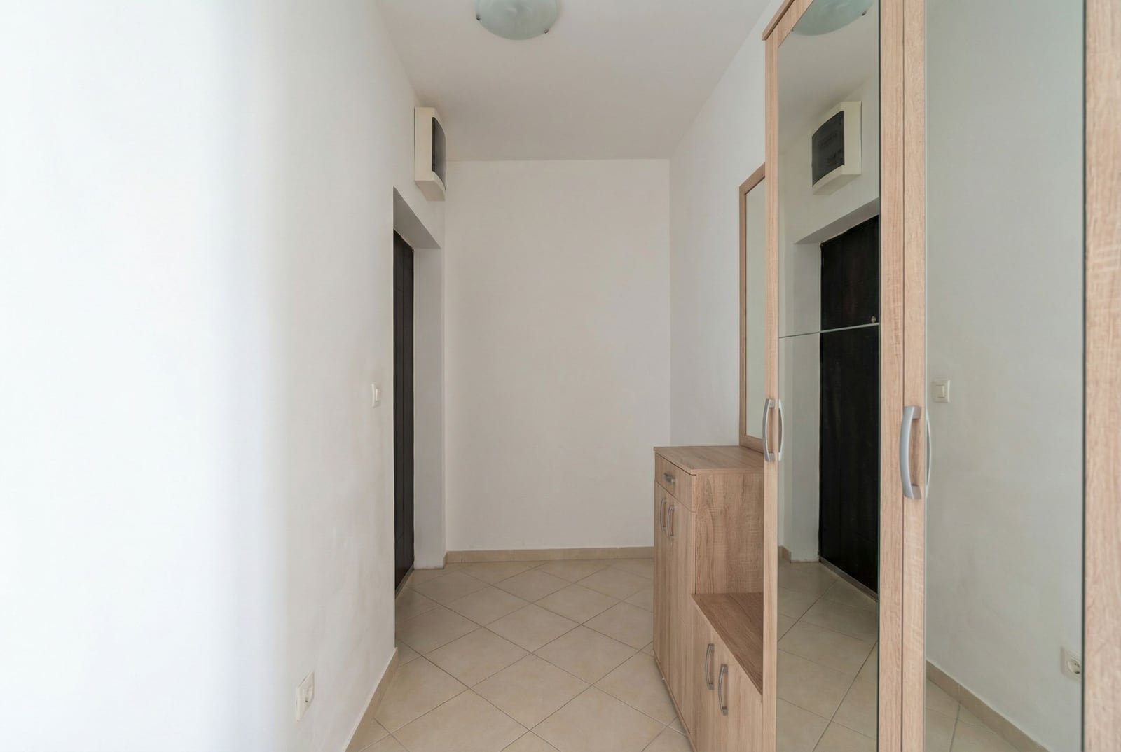 Svetao hodnik u stanu u Budvi, Crna Gora: ugradni ormar sa ogledalom, pločice na podu i beli zidovi.