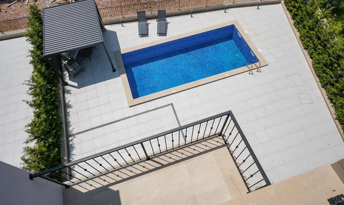 Outdoor swimming pool with sun loungers and a terrace at a villa in Rezevici, Montenegro: top view of the residential lounge area.