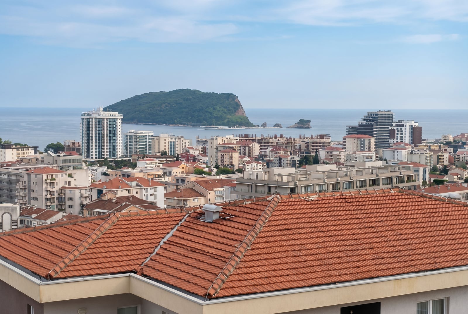 Панорамный вид на город Будва, Черногория, море и остров Святого Николая с террасы квартиры с черепичной крышей.