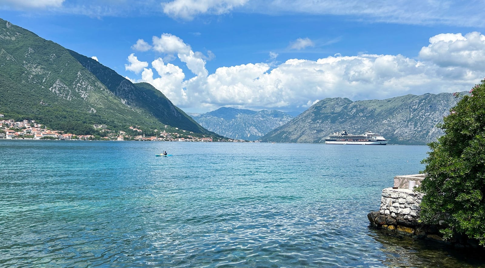 Panoramablick auf die Bucht von Kotor und die Berge vom Ufer der Villa in Dobrota, Montenegro: Meer, Kreuzfahrtschiff und Anlegesteg.