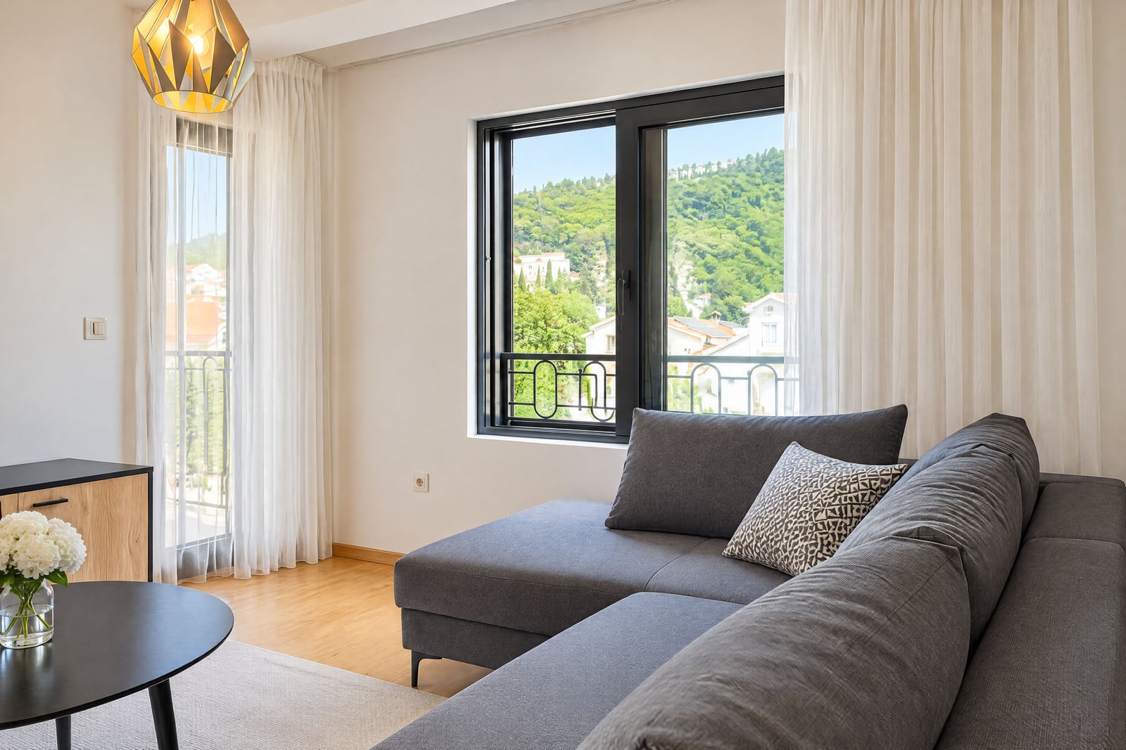 Modern living room with a gray corner sofa and panoramic mountain views in an apartment, Budva, Montenegro