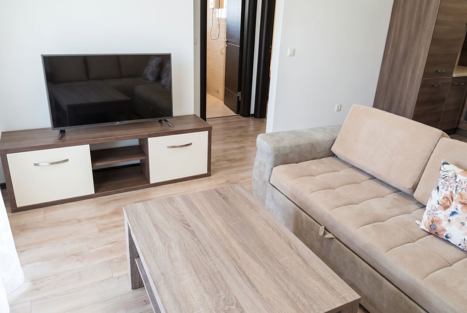 Modern living room with a beige sofa, TV stand, and light laminate flooring in an apartment for sale, Budva, Montenegro.