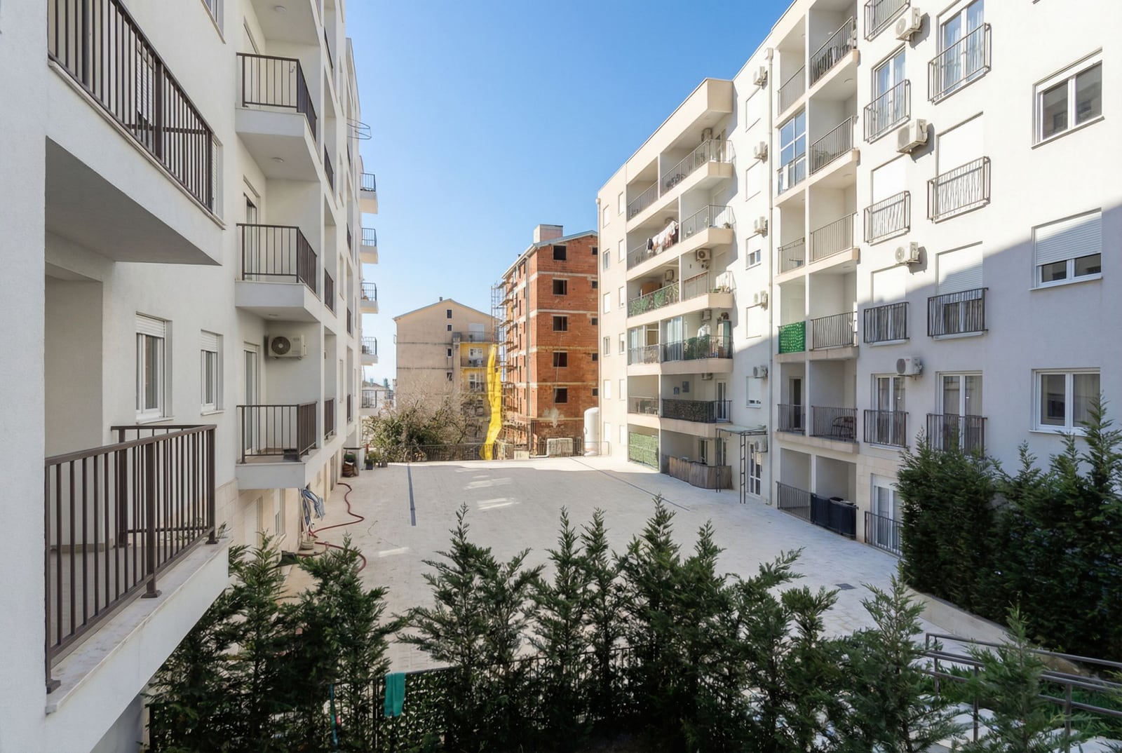 Pogled na unutrašnje dvorište stambenog kompleksa u Budvi, Crna Gora: moderne višespratnice sa balkonima i zelenilom.