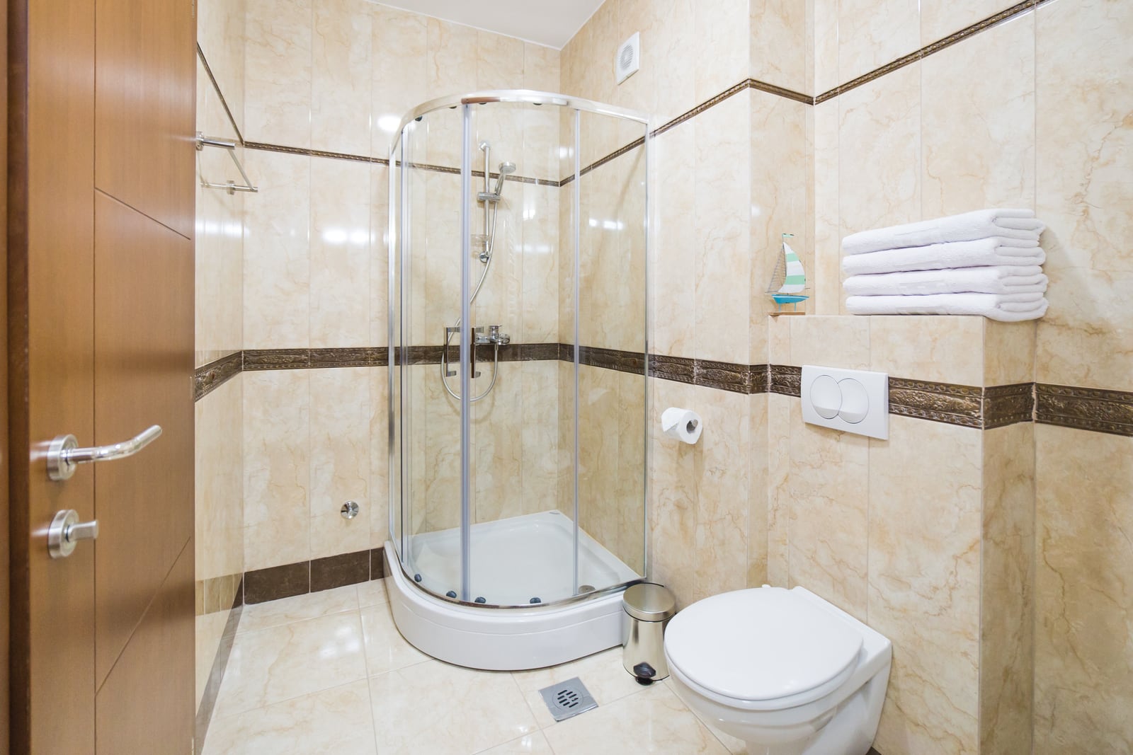Badezimmer in einer Wohnung in Bečići, Montenegro: Duschkabine, wandhängendes WC und beigefarbene Fliesen im Interieur.