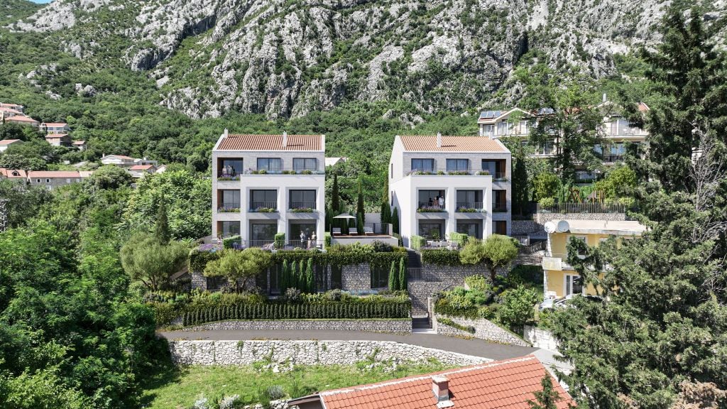 Modern three-story houses with balconies and tiled roofs against a mountain backdrop in Orahovac, Montenegro