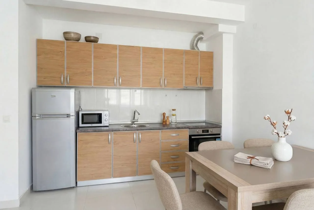 Açık renk ahşap dolapları, buzdolabı, mikrodalga fırın, tezgah ve yemek masası olan modern mutfak.