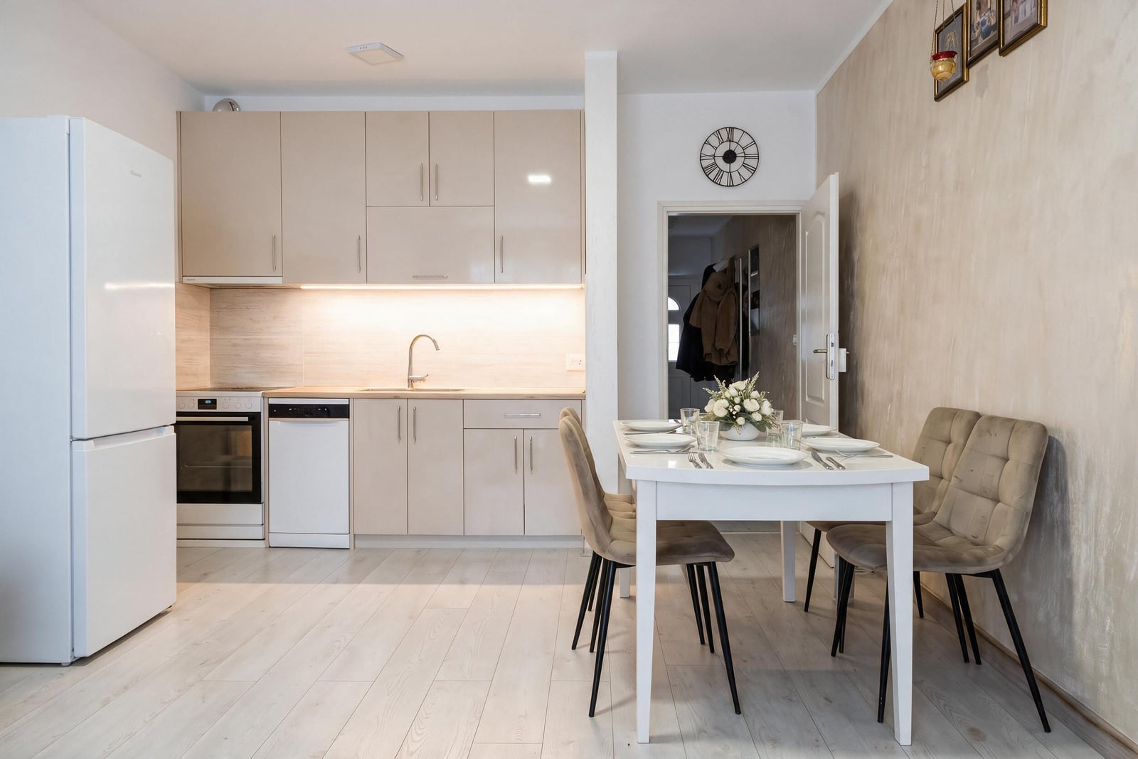 Modern kitchen with white furniture, appliances, and a dining area in an apartment in Igalo, Montenegro