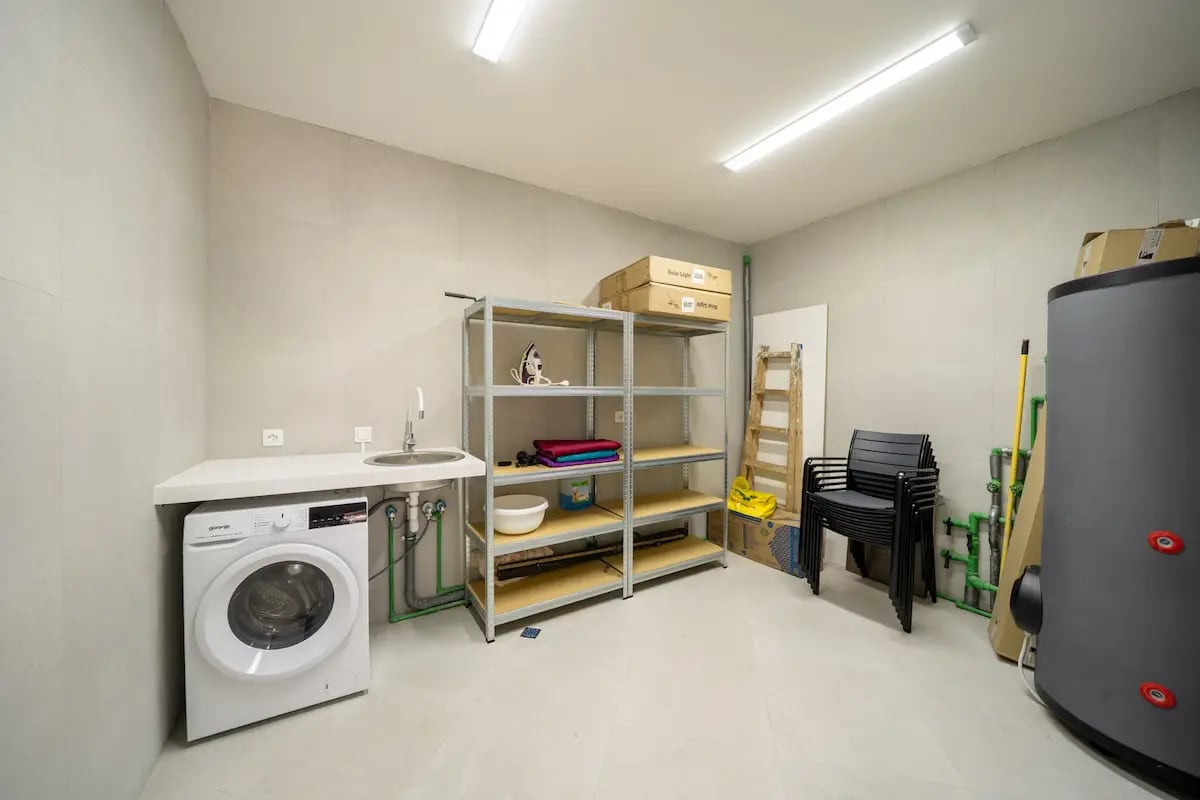 Local technique avec buanderie et chauffe-eau dans une villa à Reževići, Monténégro : lave-linge, étagère et évier.