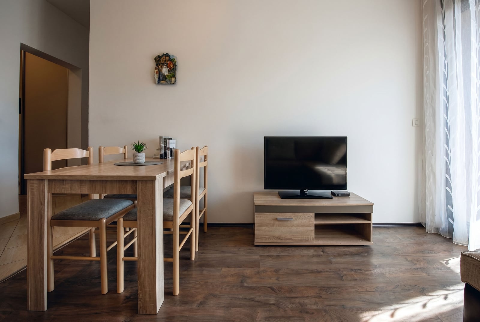 Living room with dining area and TV cabinet in an apartment, Budva, Montenegro. Light wooden furniture and laminate flooring.