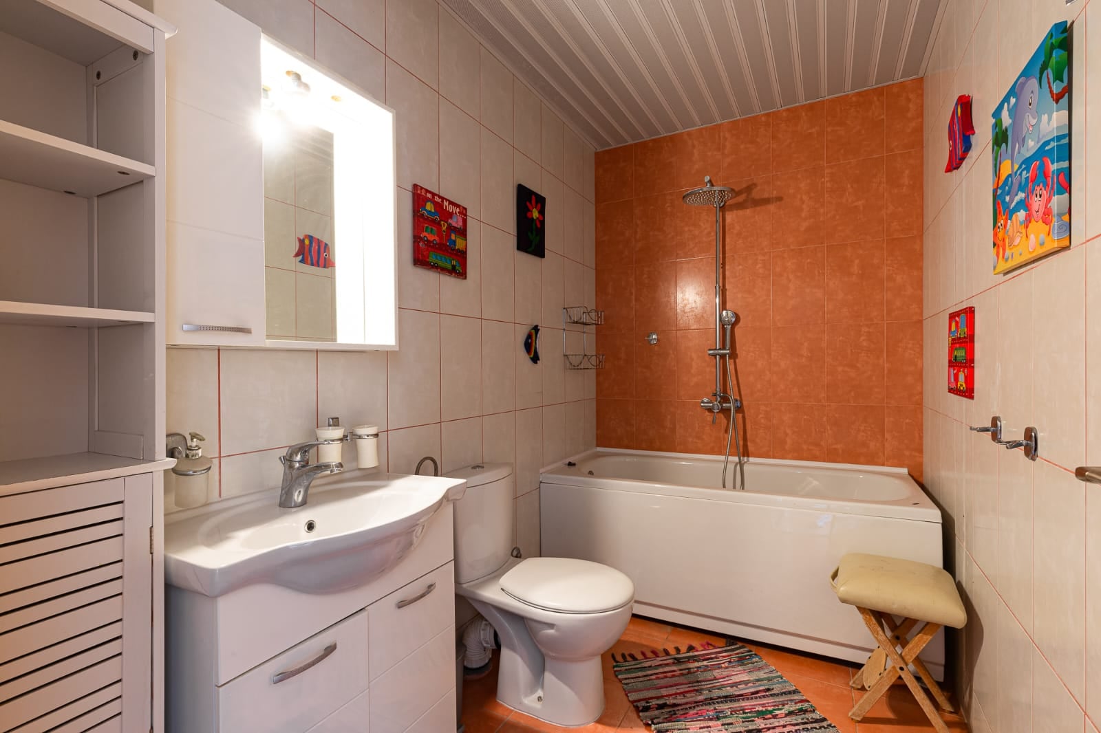 Salle de bain avec douche et mobilier blanc dans une villa à Bečići, Monténégro : intérieur avec carrelage orange et décoration.