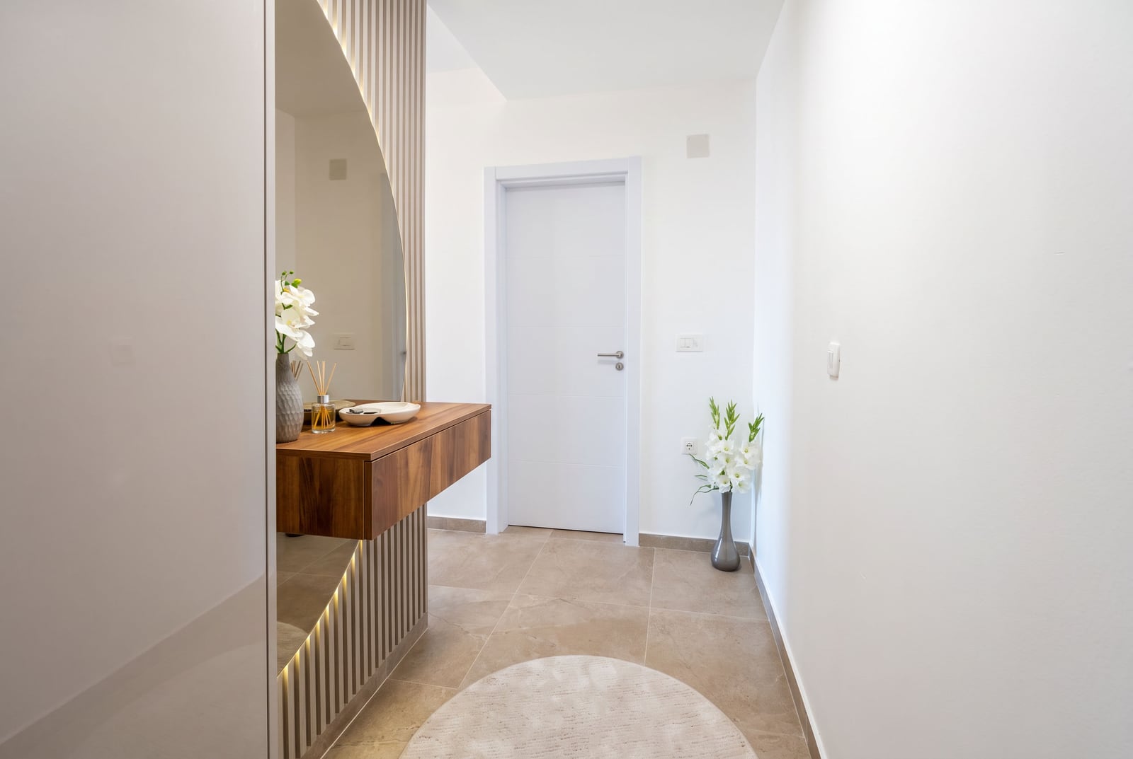 Modern bright entryway with a wooden console, a round mirror with lighting, and a white interior door in an apartment in...