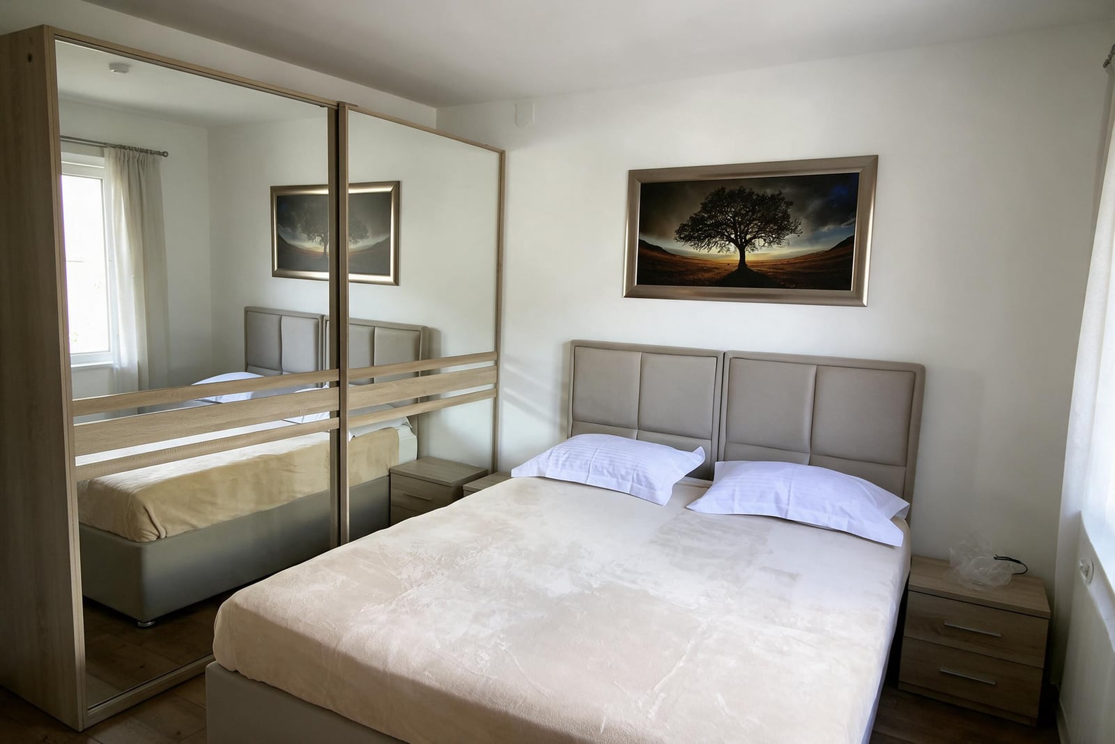 Bright bedroom in an apartment in Budva, Montenegro: double bed, nightstands, and a large mirrored wardrobe.