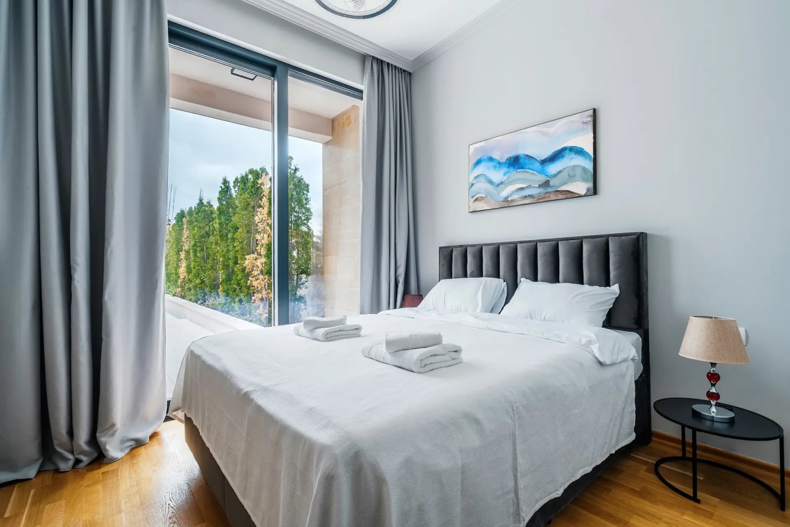 Modern bedroom with a panoramic window and garden view in a villa, Reževići, Montenegro. Double bed with a padded headboard.
