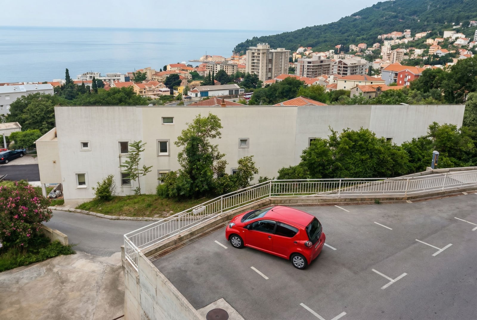 Parkplatz an der Wohnanlage in Petrovac, Montenegro, mit Panoramablick auf das Meer und die Stadtbebauung.