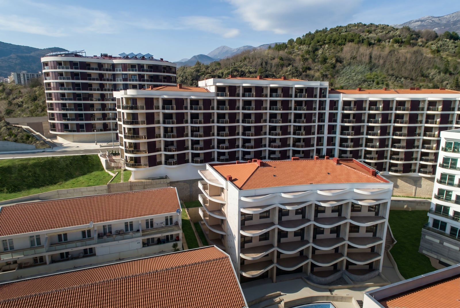 Moderner Wohnkomplex mit Terrassen in Bečići, Montenegro: Blick auf mehrstöckige Gebäude mit Ziegeldächern und die Berge.