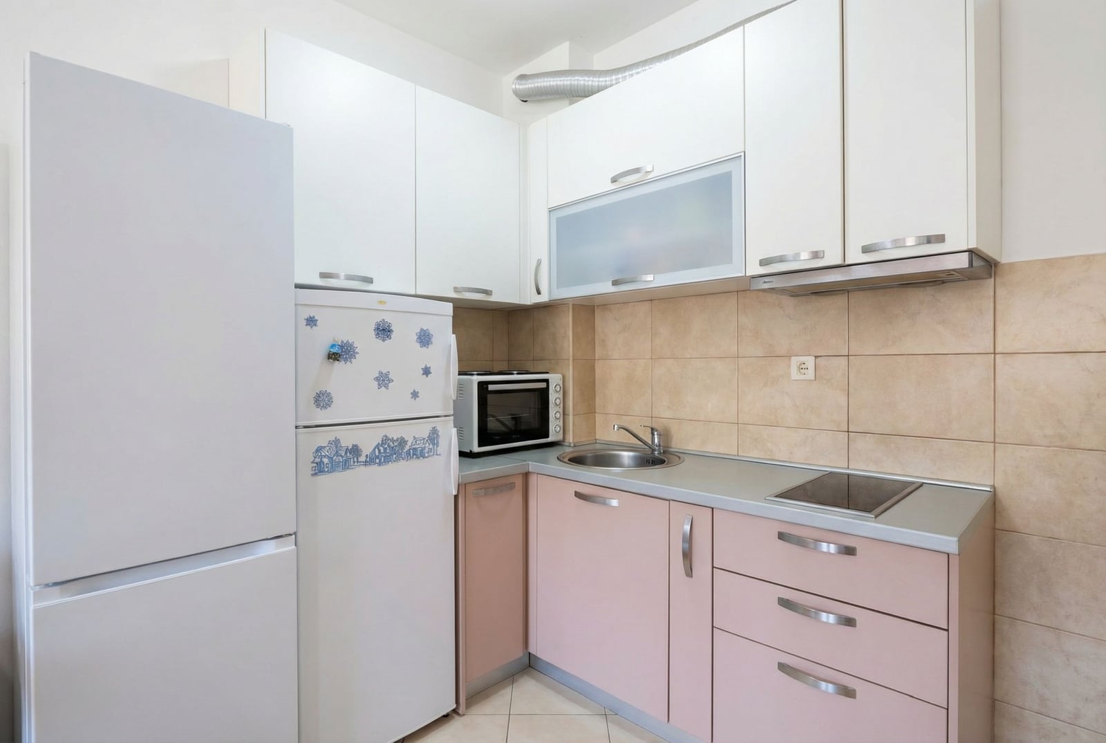 Kompaktna kuhinja u stanu u Budvi, Crna Gora: beli i roze frontovi, ugradna tehnika, pločice na zidu iznad radne površine.