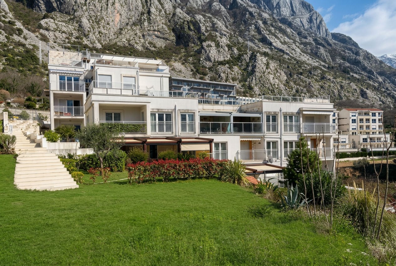 Moderna stambena zgrada sa terasama i vrtom u pozadini stjenovitih planina u Dobroti, Crna Gora