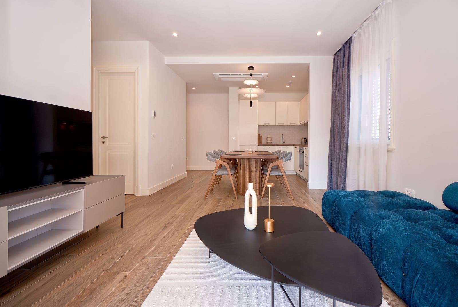 Moderner Wohnbereich mit blauem Sofa, TV-Bereich und Küche in einer Wohnung in Luštica, Montenegro