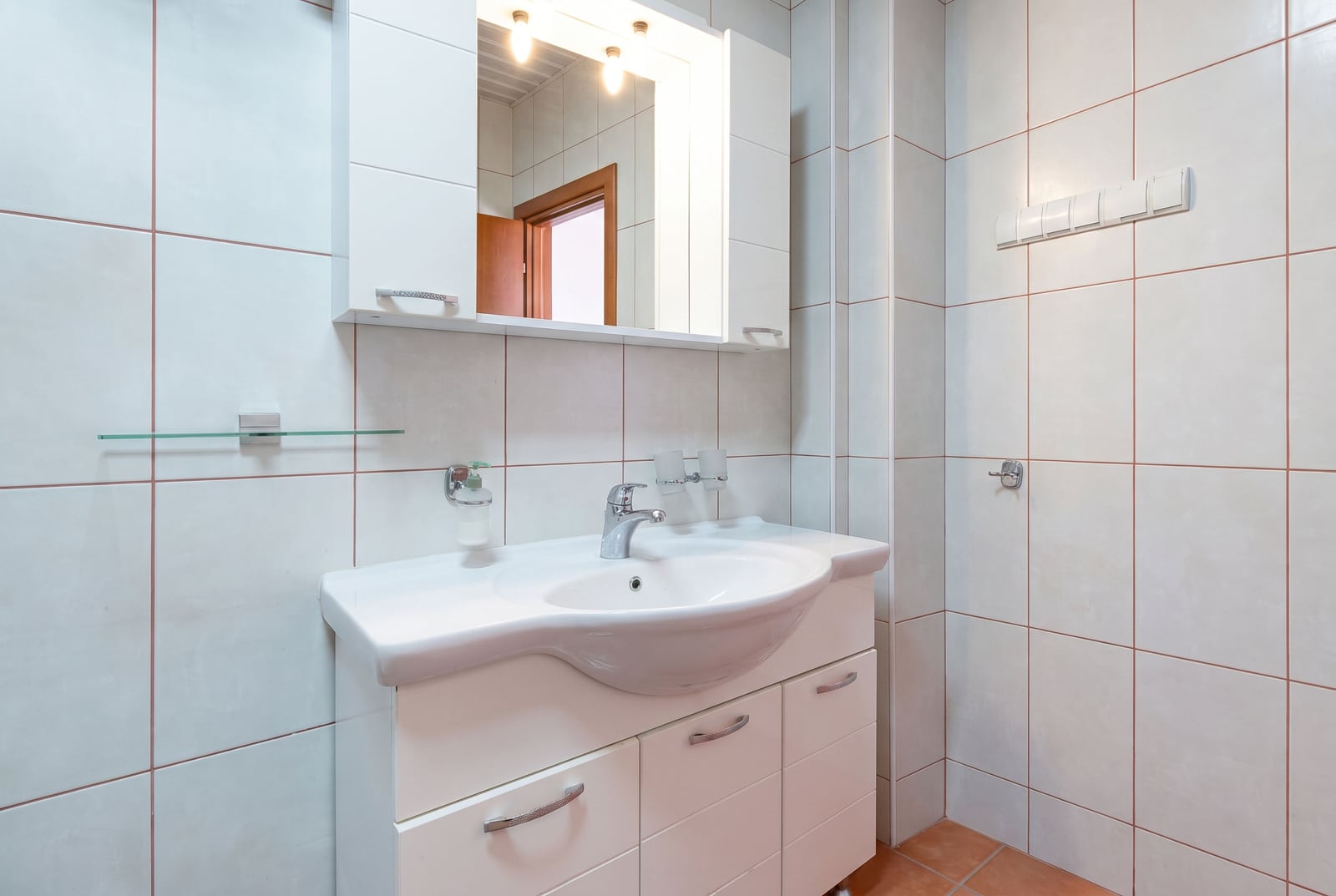 Salle de bain lumineuse avec meuble vasque blanc et miroir dans une villa à Bečići, Monténégro. Finitions modernes en carrelage.