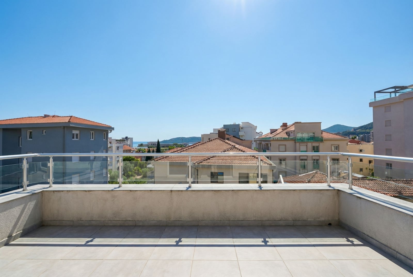 Prostran balkon s panoramskim pogledom na grad i more u stanu, Bečići, Crna Gora. Moderne staklene ograde.
