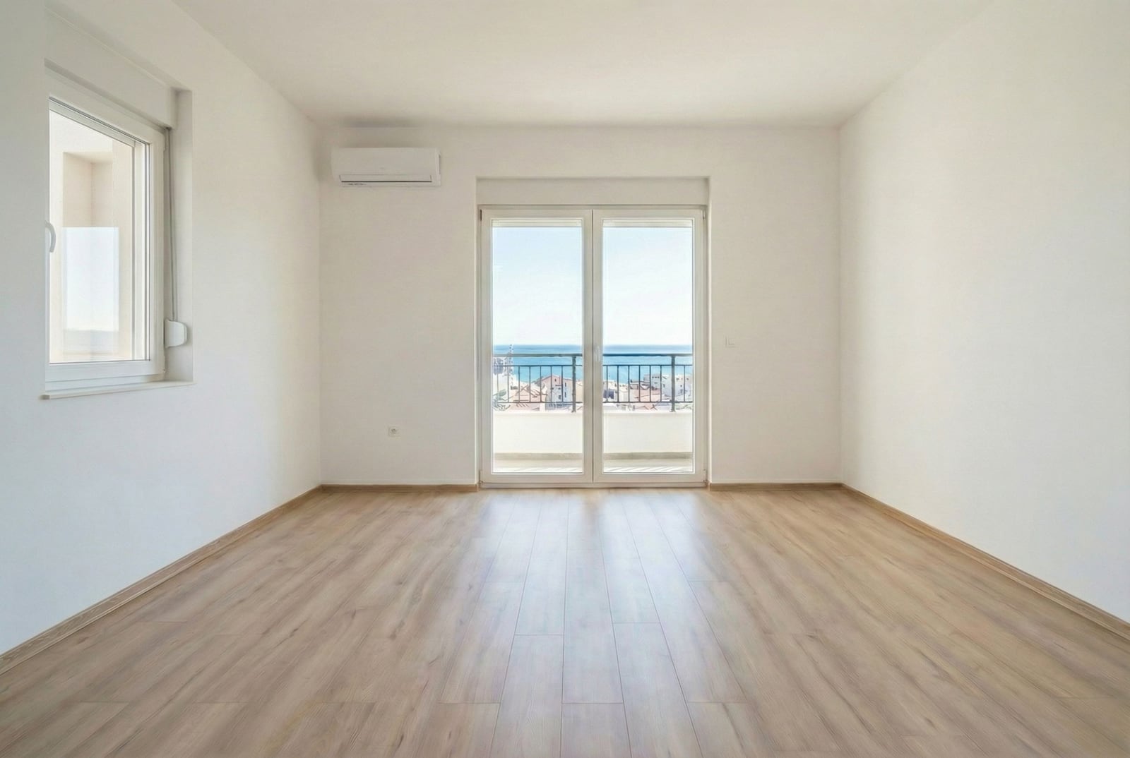 Svetla dnevna soba sa laminatom i izlazom na balkon sa panoramskim pogledom na more u stanu u Budvi, Crna Gora.
