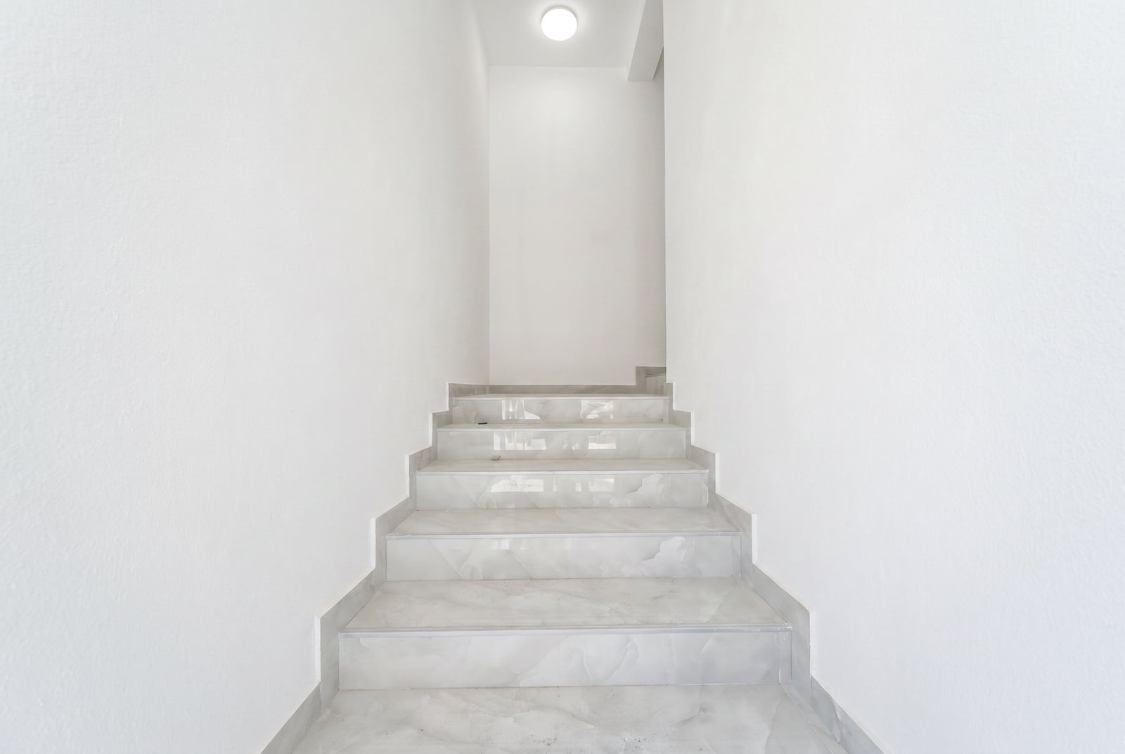Staircase with light marble finishing in a modern apartment in the city of Bar, Montenegro, with white walls.