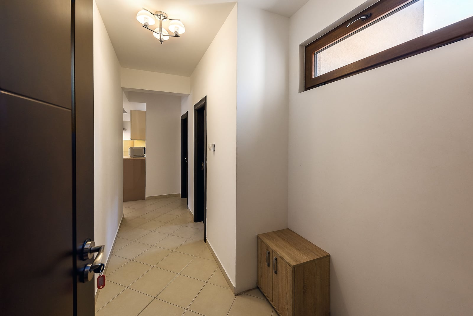 Bright hallway in an apartment in Budva, Montenegro: tiled floor, wooden cabinet, interior doors, and a view of the kitchen.
