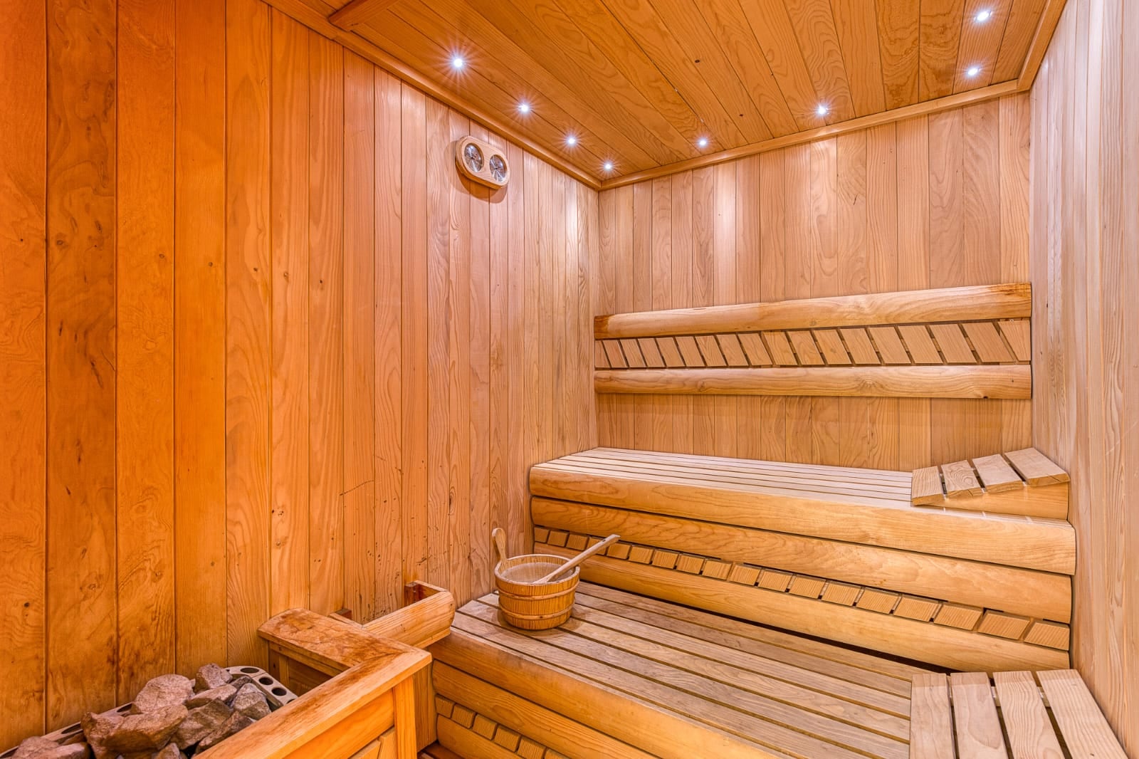 Sauna moderne en bois avec éclairage dans une villa à Bečići, Monténégro : finitions en bois, banquettes et poêle.