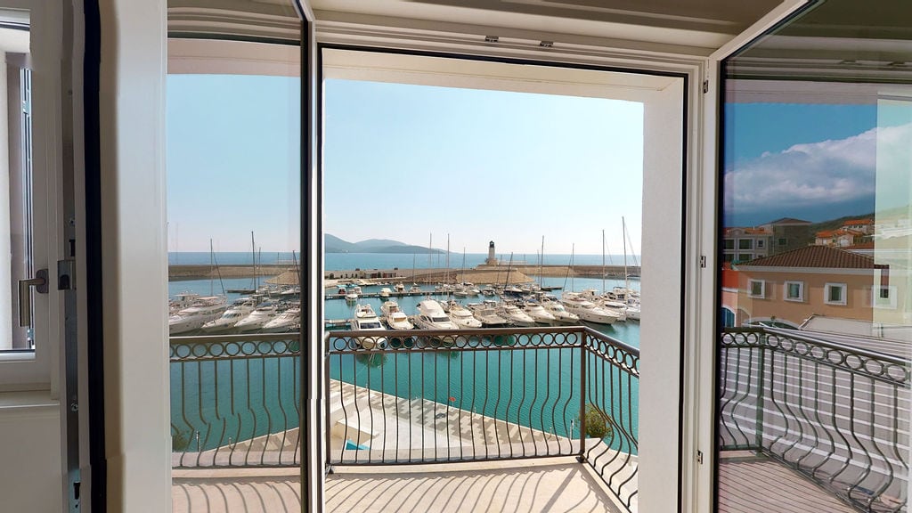 Pogled sa balkona stana u Luštici, Crna Gora: panorama na jahting marinu, pristanište i svetionik u sunčanom danu.